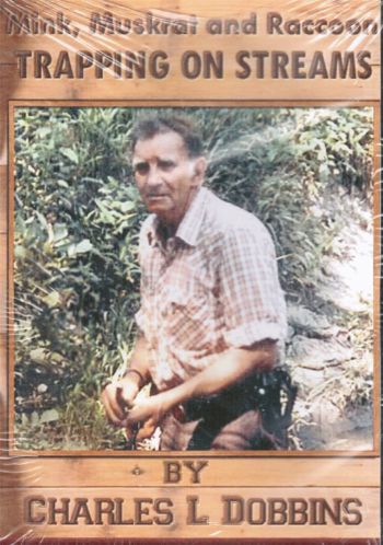 A man outdoors holds a book titled "Mink, Muskrat & Raccoon Trapping on Streams" by Charles Dobbins, surrounded by grass.