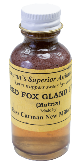 A small glass bottle labeled "Carman's Red Fox Gland Lure," containing reddish liquid, made by Carman's Superior Trapping Lures.